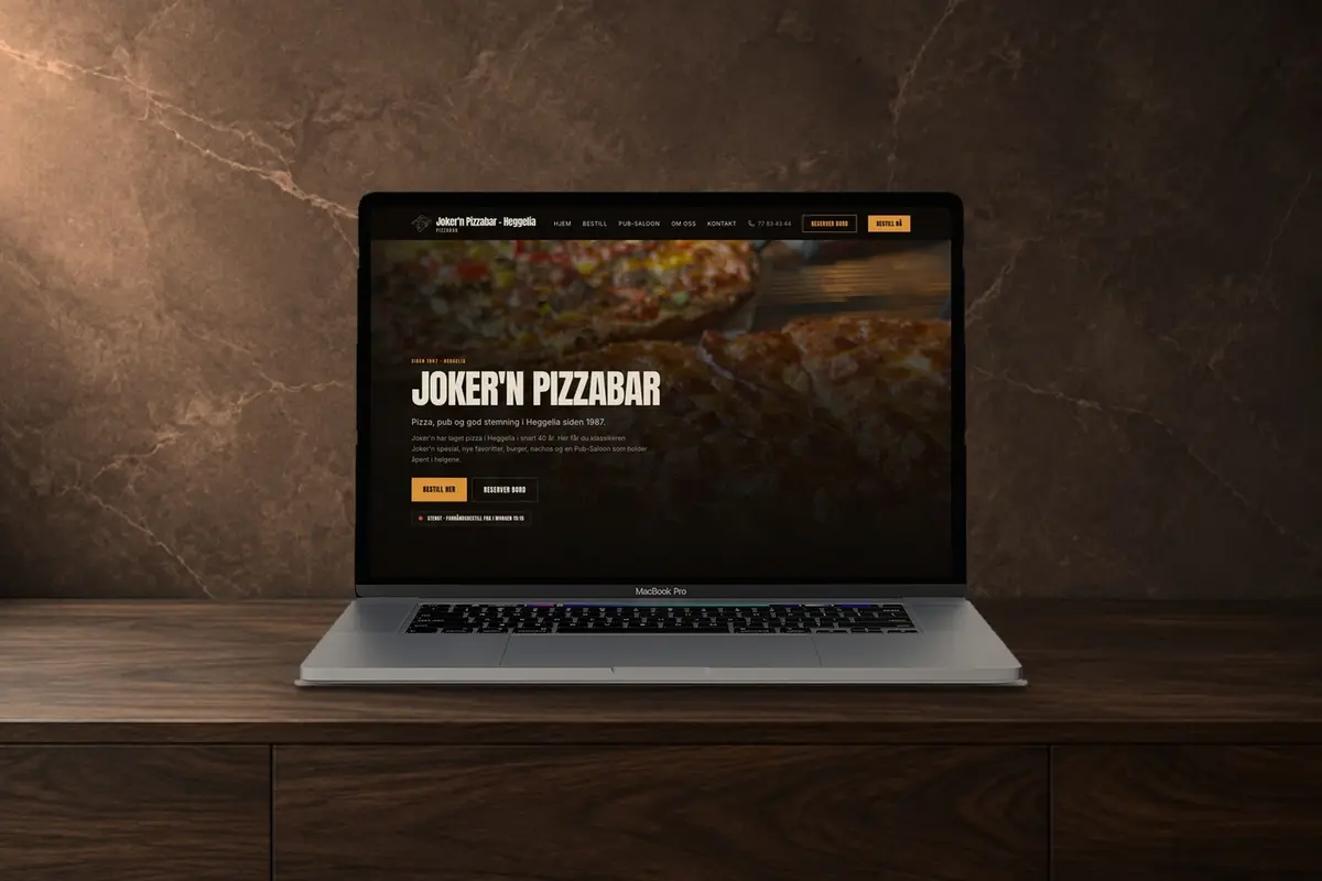 En laptop på en mørk trebenk som viser nettsiden til Joker'n Pizzabar